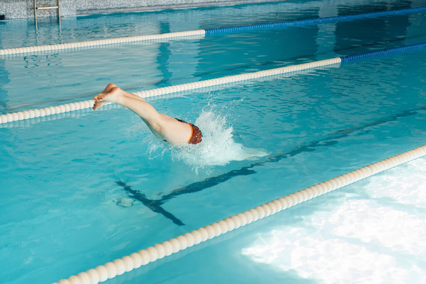 A young man dives and jumps into the water of a modern swimming pool. Training and sports development. Preparation for competitions, and a healthy lifestyle. Water treatments and a healthy lifestyle. - Foto, Imagem