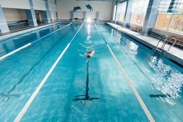 A young man trains and swims in a modern swimming pool. Sports development. Preparation for competitions, and a healthy lifestyle. Water treatments and a healthy lifestyle. - Foto, Imagem