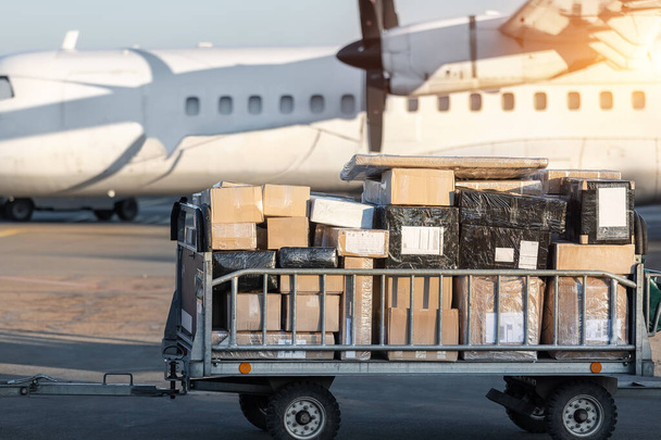 ターボプロップ貨物飛行機に対する商業小包でいっぱいの貨物カートトロリーのクローズアップ詳細ビュー。航空便の配送と物流。輸出業務をインポート。商業用チャーター便の運航 - 写真・画像