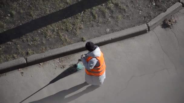 特別なスーツの女性の清掃員がほうきで通りを掃く - 映像、動画