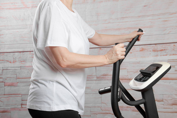 Una mujer de mediana edad está haciendo ejercicio en casa con un entrenador elíptico. Estilo de vida saludable. - Foto, Imagen