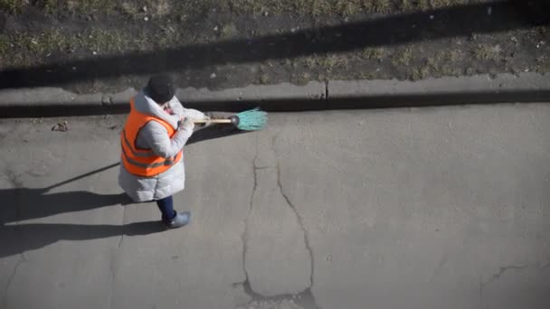 特別なスーツの女性の清掃員がほうきで通りを掃く - 映像、動画