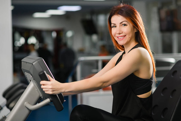 Portrait of smiling fit woman sit at gym machine for sport fitness cardio exercise, healthy active lifestyle - Photo, Image