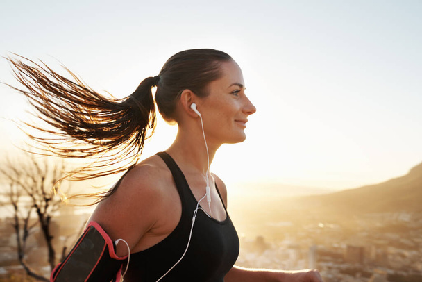 Those endorphins are kicking in. Shot of a young woman listening to music while out running. - Photo, Image