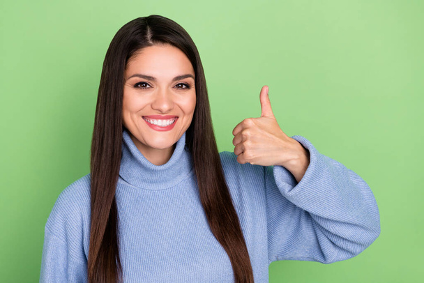 Photo of pretty adorable young woman wear blue sweater smiling showing thumb up isolated green color background - Foto, immagini