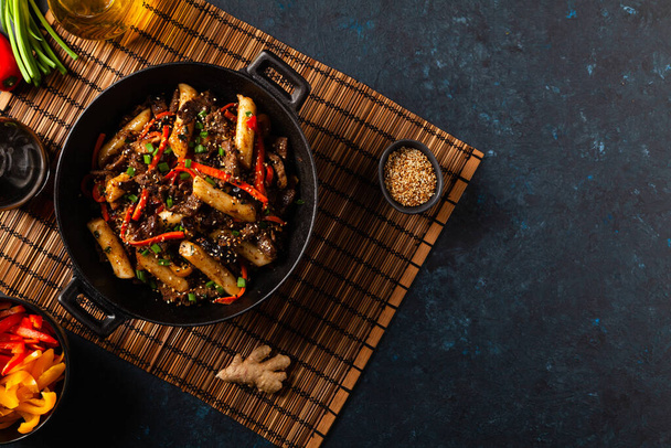 Traditional Korean Tteokbokki rice noodles with beef, vegetables and shitake mushrooms. Prepared in a wok. Dark blue background.  - Photo, Image