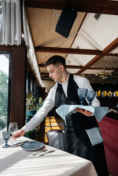 A young male waiter in a stylish uniform is engaged in serving the table in a beautiful gourmet restaurant. A high-level restaurant. Table service in the restaurant. - Valokuva, kuva