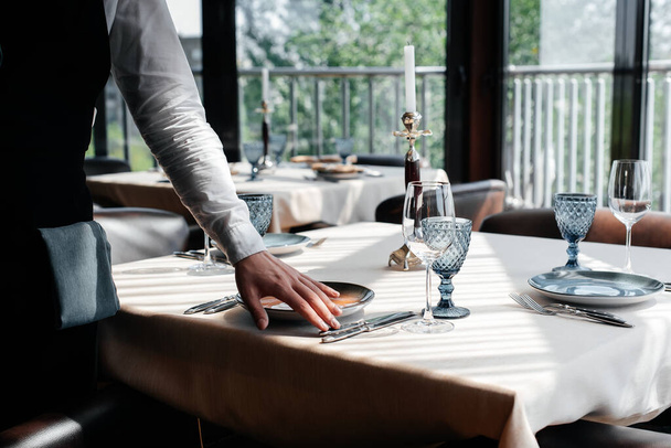 Un giovane cameriere in uniforme elegante è impegnato a servire il tavolo in un bellissimo ristorante gourmet primo piano. Servizio al tavolo nel ristorante. - Foto, immagini