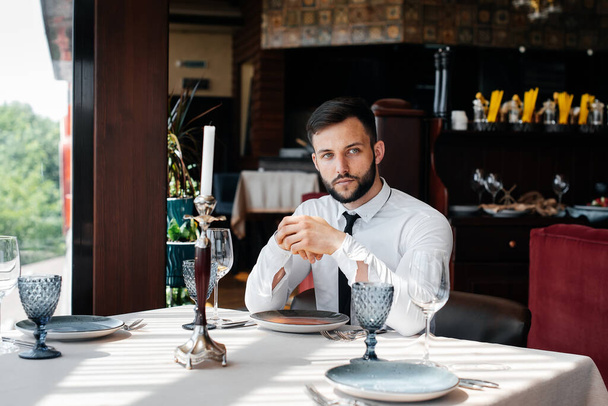 A young bearded male businessman is sitting at a table in a fine restaurant and waiting for his order. Customer service in the catering. - Photo, Image