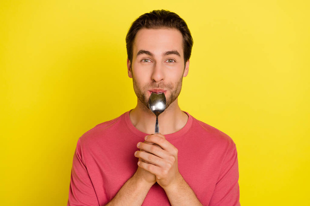 Photo of positive funny guy lick spoon enjoy delicious meal wear pink t-shirt isolated yellow color background - Zdjęcie, obraz