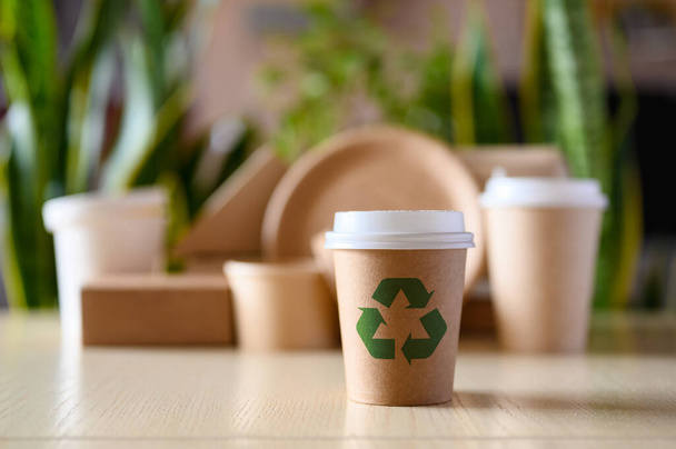 Papírpohár újrahasznosítási jelzéssel a zöld növények hátterén. A biológiailag lebomló anyagok használata az ételek előállításához a környezet védelme érdekében. - Fotó, kép