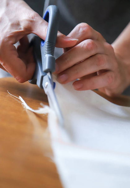 Working process of a dressmaker. Craftsperson cuts fabric with a pair of sharp scissors. Closeup photo with selective focus. - Valokuva, kuva