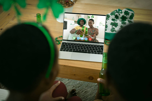 African american couple making st patrick's day video call with smiling couple on laptop at home. celebrating the irish patron saint's day at home in isolation during quarantine lockdown. - Fotó, kép