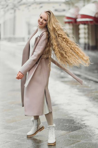 красива молода біла усміхнена жінка в бежевому пальто з довгим волоссям, що йде на відкритому повітрі
, - Фото, зображення