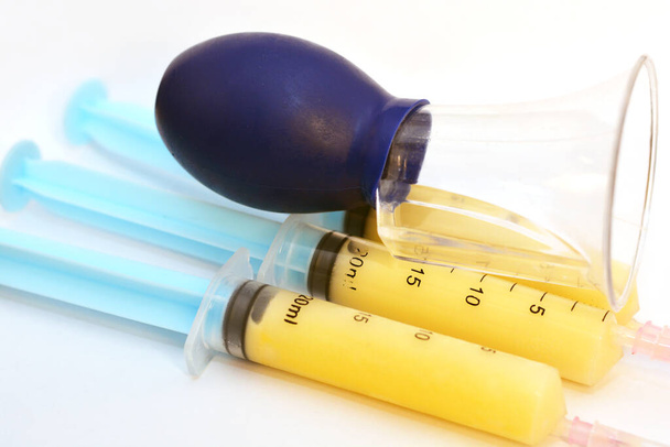 Selective focus of frozen breast milk in syringes collected by a manual breast pump prepared for feeding an infant in an incubator, syringes filled with mother milk with breast pump isolated on white  - Photo, Image