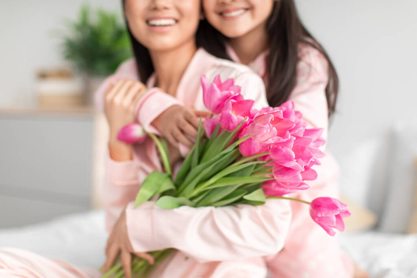 Blij tiener meisje knuffelen millennial japans dame in pyjama geven boeket van tulpen vieren moeders dag - Foto, afbeelding