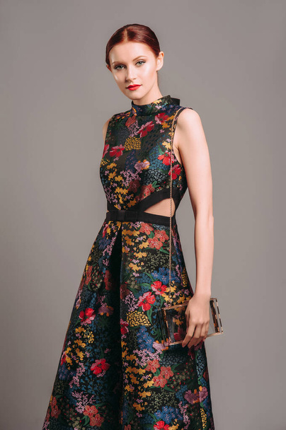 Cut out waist midi dress in floral embroidery with black high heels. Ginger lady walking in studio with transparent handbag. Evening colourful elegant gown, female fashion, gorgeous chic look. - Φωτογραφία, εικόνα