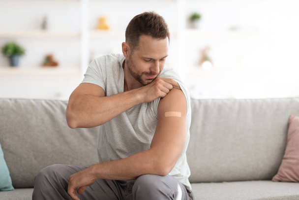 Covid-19 vakcinace. Mladý veselý běloch ukazující ramena s lékařskou omítkou po vakcinaci, prázdný prostor - Fotografie, Obrázek