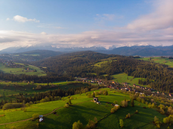 View from above on beautiful green meadows, snow-capped peaks of the Tatra Mountains in the distance. View from the air. View from the drone. - Fotó, kép