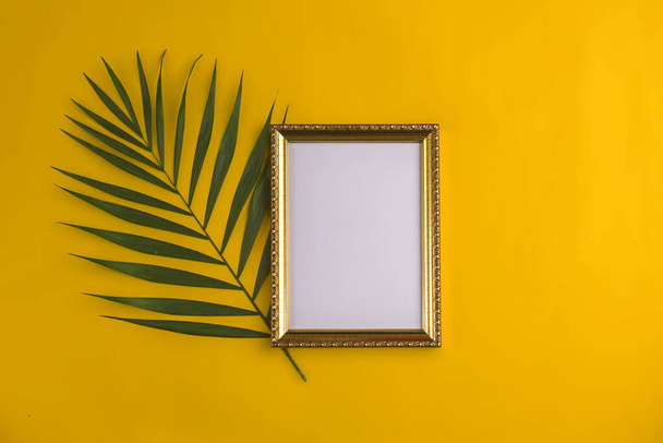 Pose plate avec cadre photo vide et branche de palmier sur fond jaune. Vue du dessus, espace de copie. Modèle de marque et de publicité - Photo, image