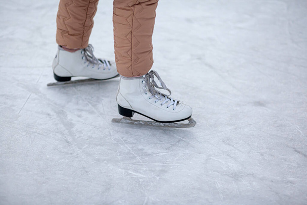 A pair of white figure skates with laces on frozen ice close-up. A man is skating. Ice skating or playing hockey in winter. ice and legs and copy space over ice background with marks from skating - Fotografie, Obrázek