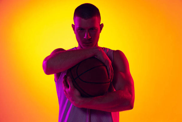 Studio shot of muscled man, basketball player, danker isolated on gradient yellow purple background in neon light. Beauty, sport, motion, activity concepts. - Foto, afbeelding
