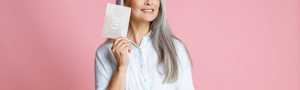 Pretty silver haired Asian woman holds gift card having ideas in studio - Fotó, kép