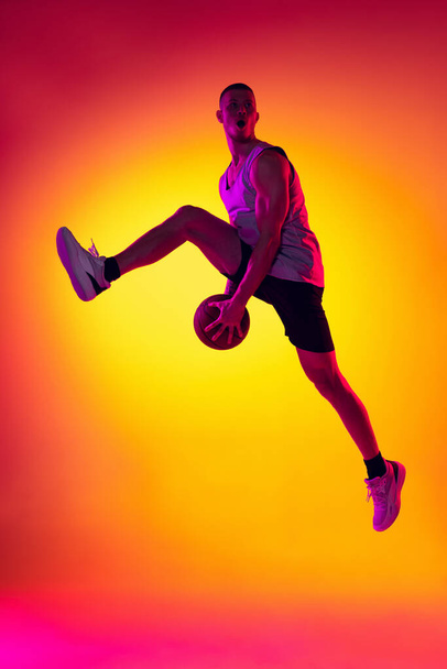 Streetballer. Male basketball player, athlete jumping with ball isolated on gradient yellow orange background in neon light. Sport, diversity, activity concepts. - Foto, Imagem