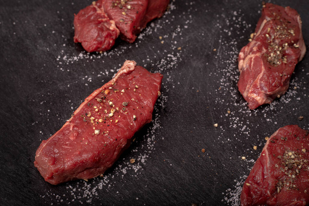 Raw beef tenderloin with salt and pepper on a black background, blackboard. Beef, game meat steaks. Red meat chops. - Photo, Image