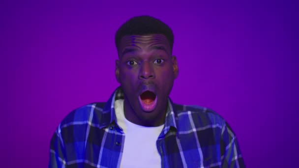 Zszokowany Afroamerykanin otwarcie usta pozowanie na fioletowy tle - Materiał filmowy, wideo