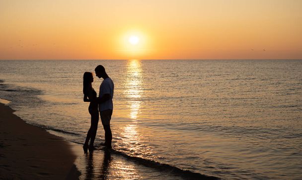恋人のカップルは、ビーチで日没時にロマンチックな柔らかい瞬間を経験しています。夏休みに若い恋人たち。愛や新婚旅行の概念です。日没時にシルエットでキス。コピースペース。旗 - 写真・画像
