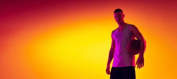 Studio shot of muscled man, basketball player, danker isolated on gradient yellow purple background in neon light. Beauty, sport, motion, activity concepts. - Fotó, kép