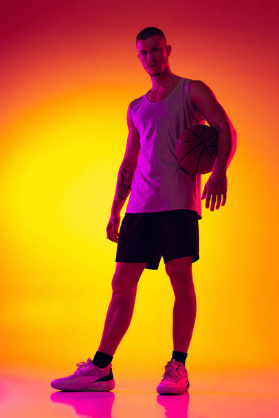 Studio shot of muscled man, basketball player, danker isolated on gradient yellow purple background in neon light. Beauty, sport, motion, activity concepts. - Фото, зображення