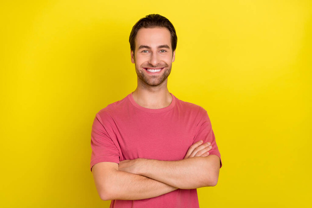 Photo of cheerful self-assured guy folded hands beaming smile wear pink t-shirt isolated yellow color background - Fotoğraf, Görsel