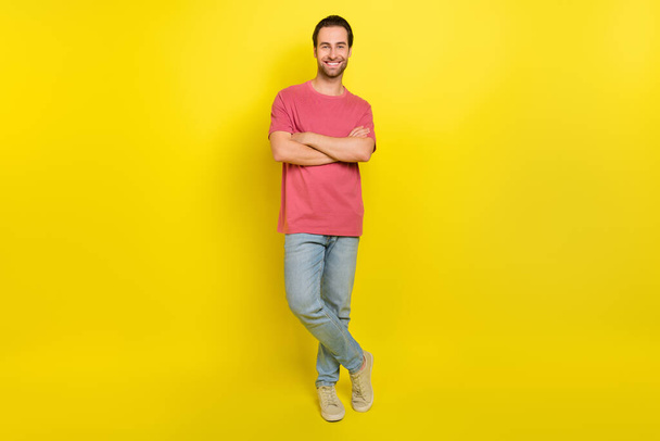 Photo of cheerful nice guy crossed arms posing wear pink t-shirt jeans footwear isolated yellow color background - Foto, afbeelding
