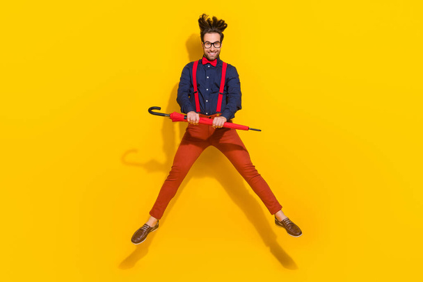 Full body photo of young excited man active energetic jumper umbrella weather isolated over yellow color background - Foto, Imagen