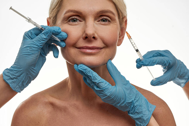 Doctors making injection on face of mature female - Photo, Image