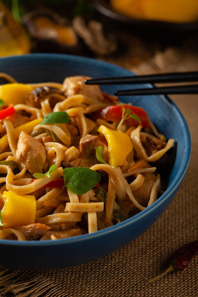 Fried chicken with mango and coconut milk with noodles. Prepared in a wok. Front view. Served in a blue bowl. - Fotografie, Obrázek