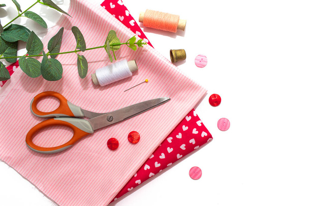 Sewing accessories, pink and red fabric on white background. Threads, needles, fabric, buttons and sewing centimeter. Copy space - Φωτογραφία, εικόνα