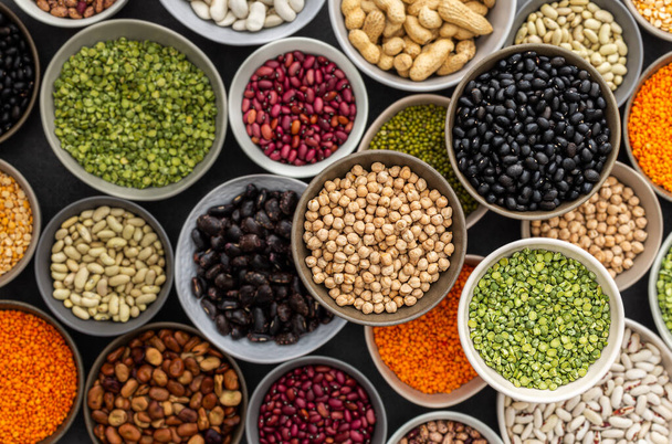 Different types of legumes in bowls, green with yellow peas and mung beans, chickpeas and peanuts, colored beans and lentils, top view - Φωτογραφία, εικόνα