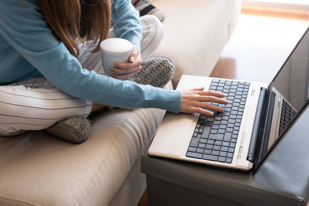 κορίτσι με ένα τσάι από βότανα στον καναπέ στο σπίτι μπροστά από την κάμερα laptop - Φωτογραφία, εικόνα
