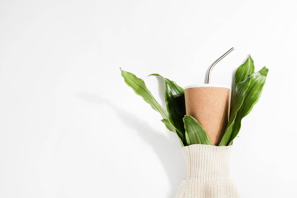reusable eco cup and branches of plant in sleeve of sweater on white background. Sustainable lifestyle, conscious consumption, concept. copy space - Photo, Image