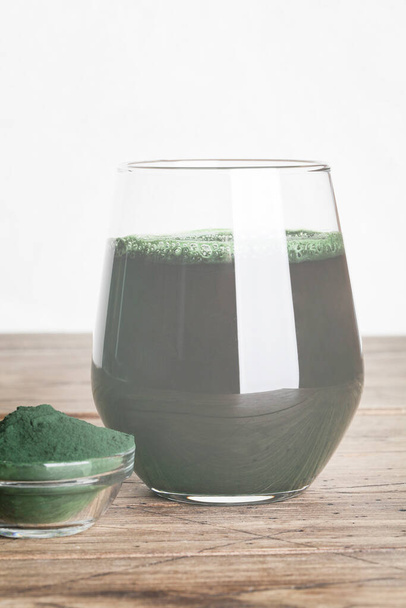 frisches grünes Getränk mit Spirulina im Glas, Spirulinapulver mit Löffel auf Holzgrund. Nützliche Gewohnheiten - Foto, Bild