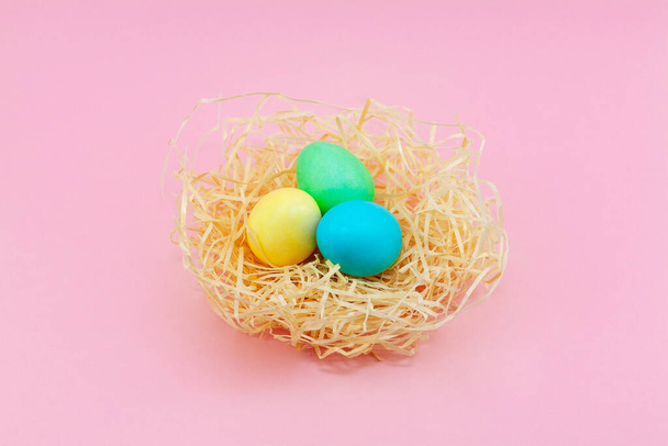 Easter eggs painted in pastel colors in hay nest against a pink background, copyspace for Happy Easter text - Fotografie, Obrázek