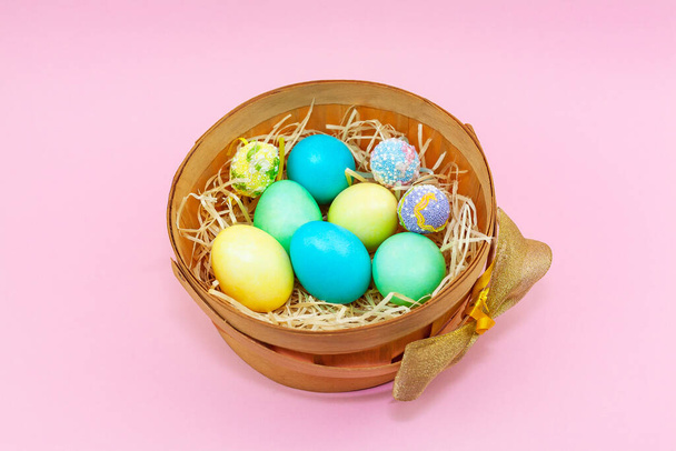 Basket of colorful Easter eggs on pink background. Pastel eggs in a basket on hay. Idea for happy easter - Foto, afbeelding