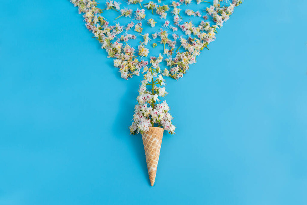 Copa de gofres crujiente dulce con flor de castaño sobre fondo azul. Los pétalos están dispersos en forma de copa de vino - Foto, imagen