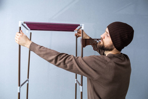 Bearded man assembles a shelf for the rack. - Фото, зображення