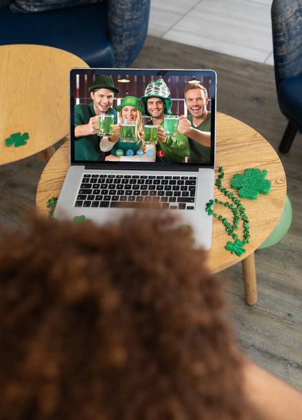Man at bar making st patrick's day video call with smiling caucasian friends in costumes on laptop. fun during celebration of the irish patron saint's day. - Фото, изображение