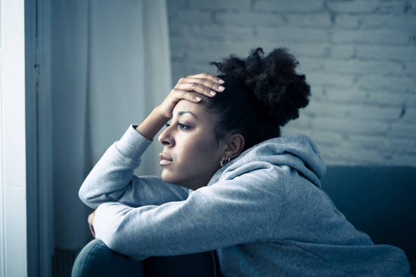 Depressed african woman with sad expression, headache and depression feeling desperate at home. Afro American teen or Attractive black young female lying thoughtful and sick on sofa in pain and worry. - 写真・画像