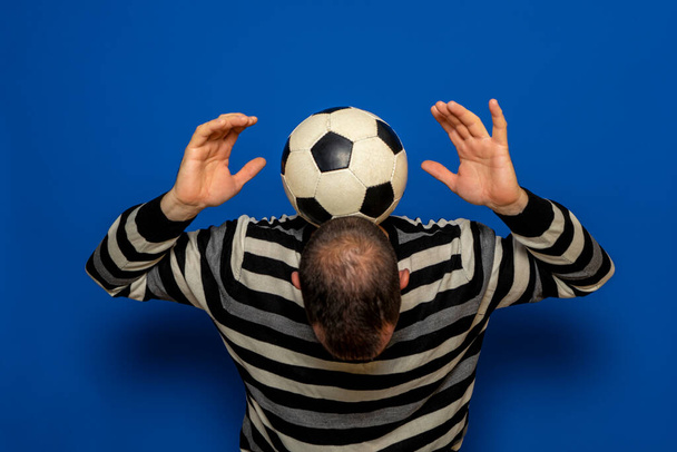 Іспанський чоловік з несамовитим листям намагається пожонглювати футбольний м'яч, він тримає м'яч на спині шиї, піднімаючи руки. Ізольований на синьому тлі - Фото, зображення